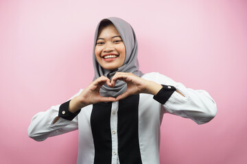 Beautiful asian young muslim woman smiling confident, enthusiastic and cheerful with hands sign of love, affection, happy, on chest isolated on pink background