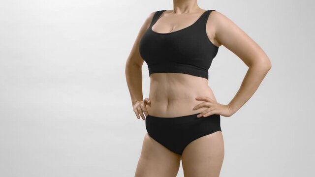 Obese woman model in black bra and briefs demonstrating how good and bad posture affect appearance. Instruction how to mask excess weight. Still studio video shot of body parts.