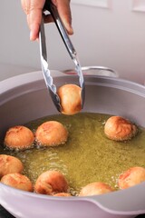 A Women Pick Up Mini Donut from Hot Oil with Stainless Tongs.