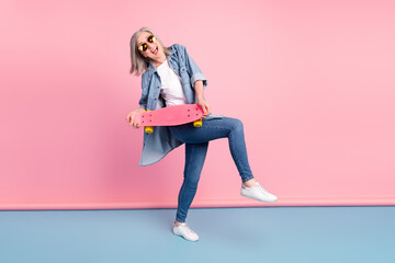 Full body photo of positive charming old woman hold longboard smile isolated on pastel pink color background