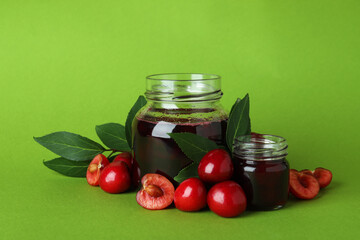 Cherry jam and ingredients on green background