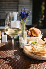 Glass of cold white wine and oven baked camembert cheese with rosemary on baking paper on wooden plate. Serving lunch at the winery, rustic style table setting