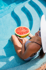 Overhead view of smiling woman in sunglasses holding watermelon in pool