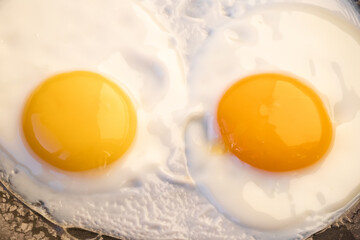 Cooked tender, soft fried eggs with two bright round raw yolks in whites in a black frying pan. Simple breakfast. Top view, close-up. Look like eyes