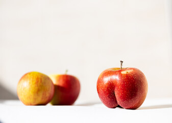 Bright ripe red apple of an unusual shape in the light of the sun on a white background with two...
