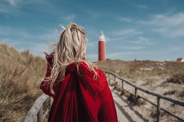 close-up blonde girl in a red sweater, hair developing in the wind, rear view, on texel island...