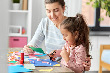 Obraz na płótnie Canvas family, art and craft concept - mother spending time with her little daughter making applique and cutting color paper with scissors at home