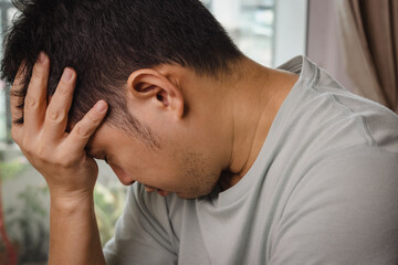 Closeup of adult Asian man is sitting with hand at his head because of headache and depress from...