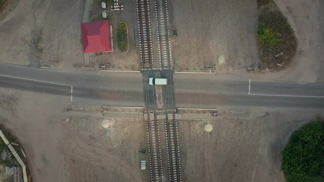 White car crosses the rails at an automatic railway crossing, aerial drone top view. Moving railway rails outside the city.