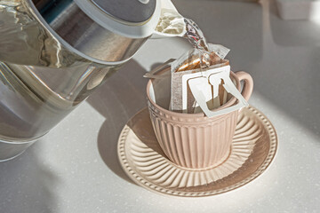 Drip brewing coffee. Pouring hot water into cup with drip coffee bag on white marble table, closeup