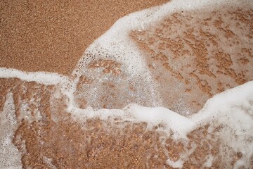 Ocean foamy wave on the sandy beach background    