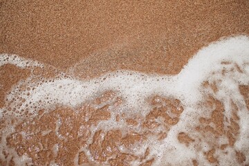 Ocean foamy wave on the sandy beach background    