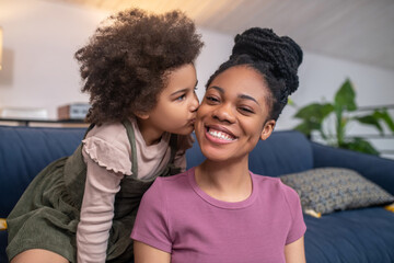 Little girl kissing happy mom on cheek