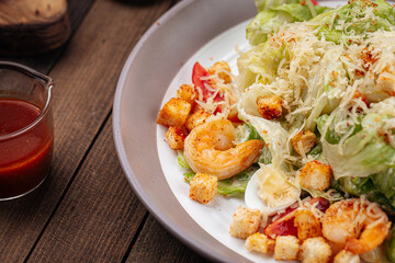 Caesar salad with shrimp and croutons on wooden background