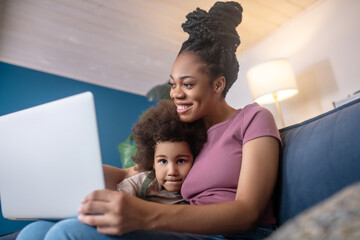 Embracing mom and little girl looking at laptop