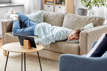 people, boredom and depression concept - bored or lazy young man with tablet pc computer lying on...
