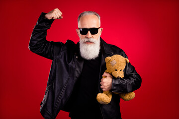 Photo of aged man serious confident ear eyeglasses hold hand strong protect teddy bear toy isolated over red color background