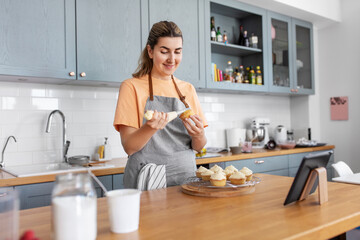 culinary, bake and cooking food concept - happy smiling young woman with baking bag making cupcake...