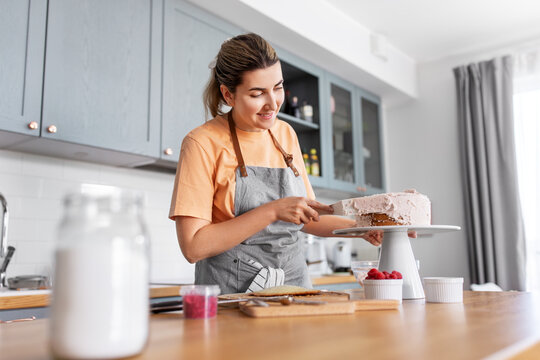 culinary, baking and cooking food concept - happy smiling young woman making layer cake and spreading topping cream on kitchen at home