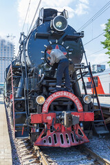 Worker washes a black retro steam locomotive on the railway platform of the Rizhsky station. Moscow, Russia