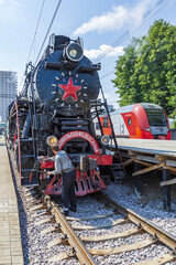 Fototapeta premium Worker washes a black retro steam locomotive on the railway platform of the Rizhsky station. Moscow, Russia