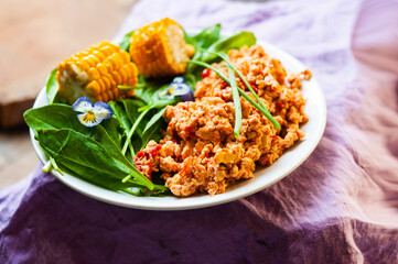 Vegan scrambled eggs dish with green and corn colorful tasty flat lay top view violets flower decoration food styling inspiration plant based food
