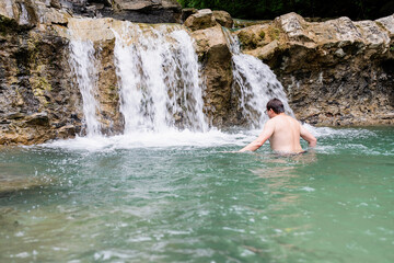 Fototapeta na wymiar Man swimming in the mountain river with a waterfall