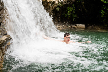 Man swimming in the mountain river with a waterfall