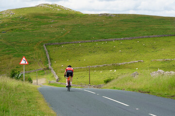 Cycling Along a scenic country road, a man is facing a big hill ahead of him as he makes his way along the road in the Yorkshire Dales, North Yorkshire, England, UK. - Powered by Adobe