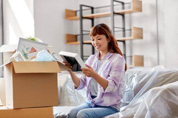 moving, people and real estate concept - happy smiling asian woman unpacking boxes at new home