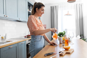 culinary, drinks and people concept - happy smiling young woman making orange cocktail at home kitchen - obrazy, fototapety, plakaty