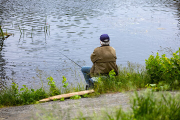 Fishing as a hobby. A man fishing with a fishing rod on the shore of a pond, river or lake, will spend his free time.