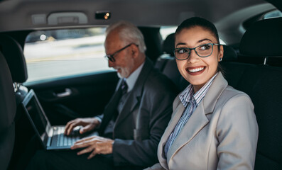 Fototapeta na wymiar Good looking senior business man and his young woman colleague or coworker sitting on backseat in luxury car. Transportation in business concept.