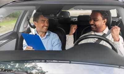 driver courses, exam and people concept - happy smiling indian man and driving school instructor with clipboard in car