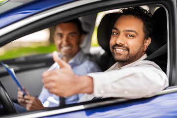 driver courses, exam and people concept - happy smiling indian man showing thumbs up and driving school instructor with clipboard in car