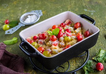 Clafoutis with gooseberries, a French dessert made from baked pancake dough in a portioned black mold on a green concrete background. Gooseberry recipes.