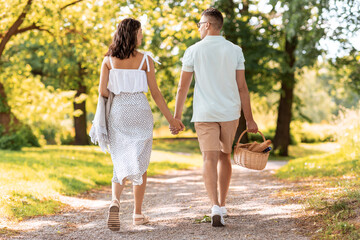 Obraz premium leisure, vacation and people concept - happy couple with picnic basket and blanket walking at summer park