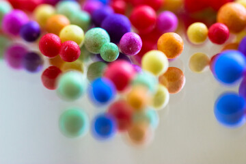 Foam polystyrene round bright colorful beads are reflected on a surface of a glass, mirror. Multicolored pearls floating down, hanging in the air. Foam spherical background. Celebration, fun concept.