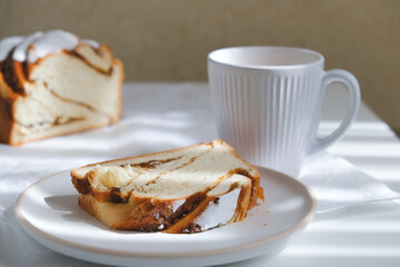 Cinnamon roll or cinnamon bun Dessert on plate with white cup of coffee. sunshine and shadows 