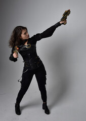 Full length portrait of young woman with natural brown hair,  wearing black leather scifi outfit with corset, standing pose on light grey studio background.
