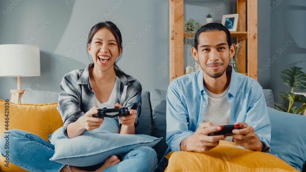 Sticker Happy asia young couple man and woman sit on couch use joystick controller play video game spend fun time together in living room. Asian married couple family lifestyle, Couple stay at home concept.