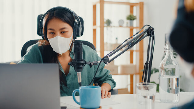 Asia girl radio host record podcast use microphone wear headphone interview guest content wear mask protect virus conversation talk and listen in her room. Podcast from home, coronavirus quarantine. - Powered by Adobe