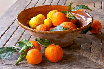 Fresh oranges and lemons with green leaves in a rustic bowl on a wooden table, Majorca or Mallorca.