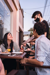 A young waiter wearing a face mask in a bar recommends the menu of the day.