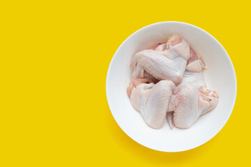 Fresh raw chicken wings in white bowl on yellow background.