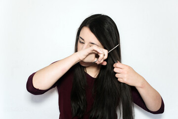 Beautiful brunette woman cutting her long hair with scissors on a white background