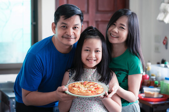 The happy family consisted of father, mother and daughter holding homemade pizza pans in the home kitchen