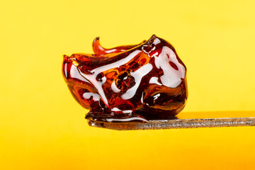 large piece of cannabis wax on a yellow background close-up, resin dab on scrape stick