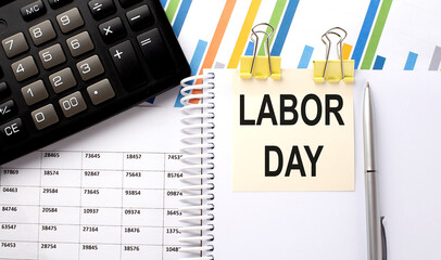 LABOR DAY text, written on a sticker with calculator,pen on the chart background.