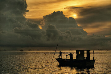 Silhouette of a fishing boat in the ocean with dramatic giant clouds in the background at sunset © Yudhy Ariyantho/Wirestock